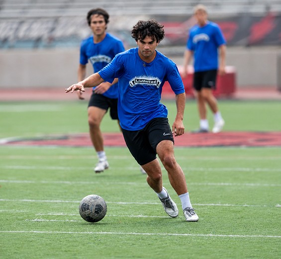 Men's athlete dribbling past a defender in a red jersey